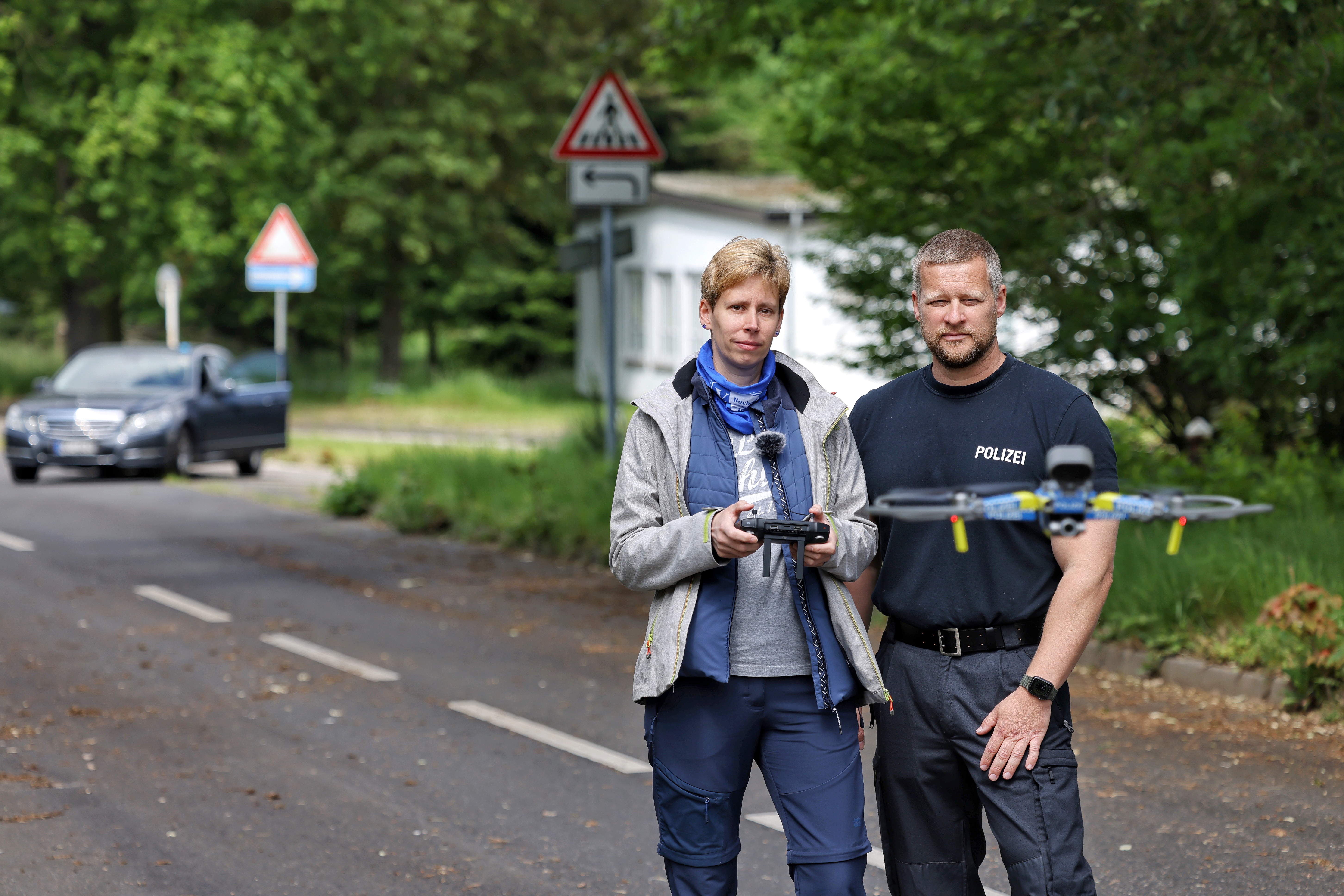 Zwei Personen stehen auf einer Straße, vor ihnen fliegt eine Drohne in der Luft.