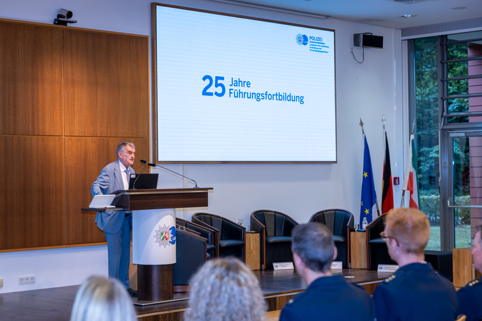 Der Minister des Innern des Landes NRW steht an einem Rednerpult und spricht zu einem Publikum.